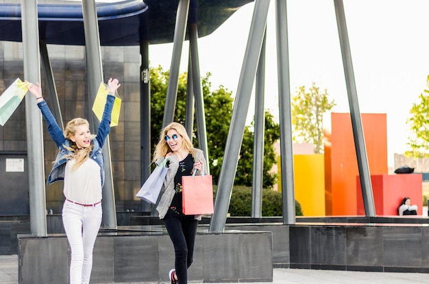 Foto 2 dos amigas de compras con bolsas en el centro comercial al aire libre