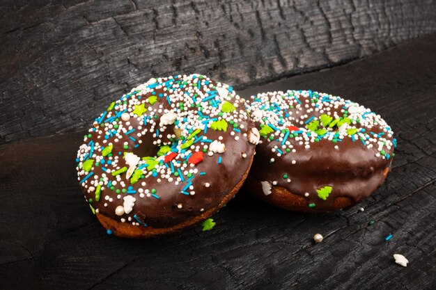 2 glasierte Schokoladen-Donuts auf dunklem Hintergrund gestreut. süßes leckeres Brötchen.