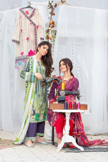 2 hermosas chicas posando junto con una vieja máquina de coser con un vestido de diseñador tradicional