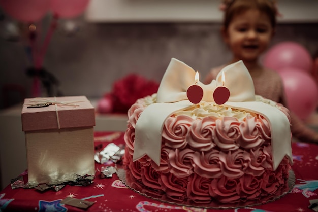 2-jähriges Mädchen in rosafarbenem Kleid mit ihrem ersten Geburtstagskuchen, alles Gute zum Geburtstagskarte, ein süßes kleines Mädchen feiert ihren ersten Geburtstag, umgeben von Geschenken