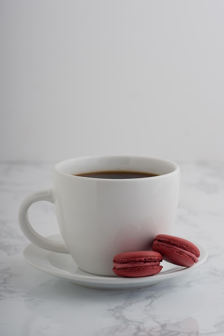 Foto 2 macarrões franceses com uma chávena de café numa mesa de mármore