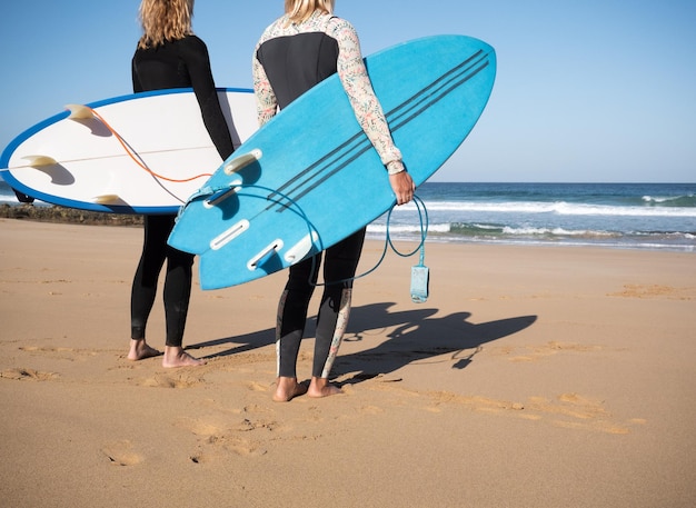 2 nicht erkennbare Surferinnen beobachten die Wellen am Strand