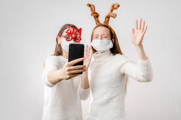2 niñas o mujer joven con gorro de Papá Noel y mascarilla haciendo videollamadas en línea. Cuarentena