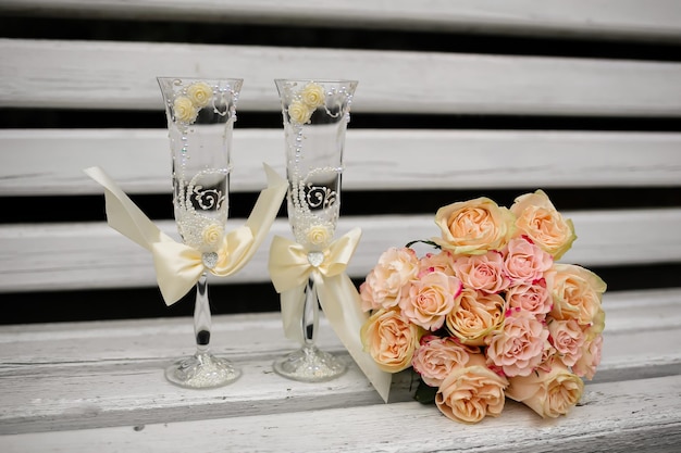 2 taças de champanhe e um buquê de noiva perto do restaurante em um banco branco. É outono lá fora.