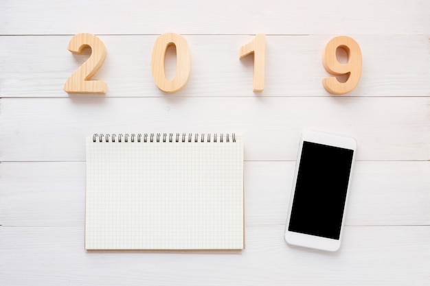 2019 letras de madera, papel de cuaderno en blanco, teléfono inteligente con pantalla en blanco