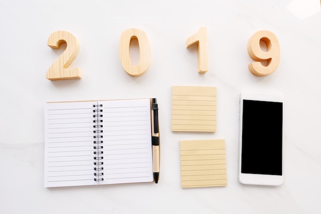 2019 letras de madera, papel de nota en blanco, teléfono inteligente sobre fondo blanco