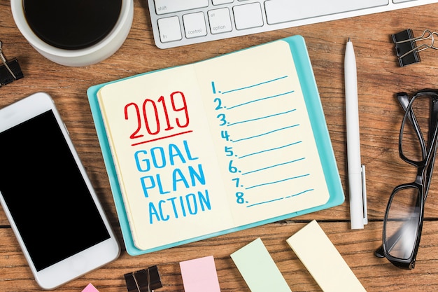 2019 Ziel des neuen Jahres, Plan, Aktionstext auf Notizblock mit Bürozubehör.