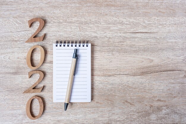 2020 feliz año nuevo con cuaderno de papel, bolígrafo y número de madera