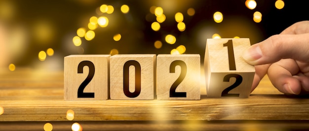 De 2021 a 2022, concepto feliz año nuevo. Cambio de mano de bloques de madera en la mesa, fondo bokeh.