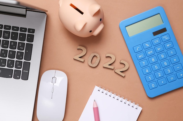 2022 e laptop Calculadora de mealheiro em fundo marrom Composição do ano novo da economia Plano orçamentário do ano