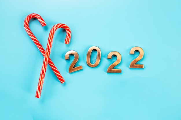 2022 goldene Figuren, Zahlen, Zuckerstange und Gnome oder schwedischer Tomte, auf blauem Hintergrund. Frohes neues Jahr. Goldzahlen, Feiertagshintergrund, Postkarte, Party. Glänzende Zahlen, Kopienraum