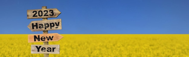 2023 feliz año nuevo escrito en una señal de dirección frente al campo de colza amarilla que florece bajo los colores del cielo azul de la bandera ucraniana
