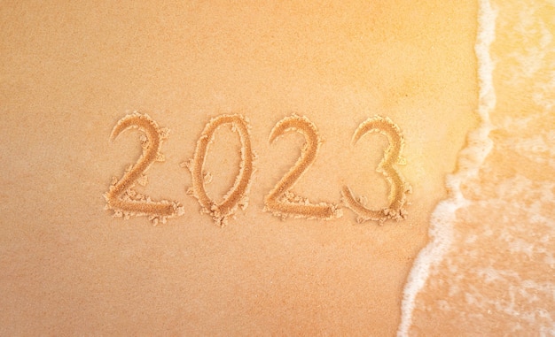 2023 figuras en la playa de arena en el fondo La ola del mar de Nochevieja se lleva la inscripción 2023 en el primer plano de arena amarilla Vacaciones de año nuevo en la playa