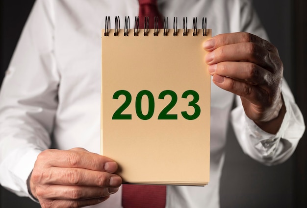 2023 neujahr auf papierseite des tagebuchnotizbuches in den karrierevorsätzen der geschäftsmannhand
