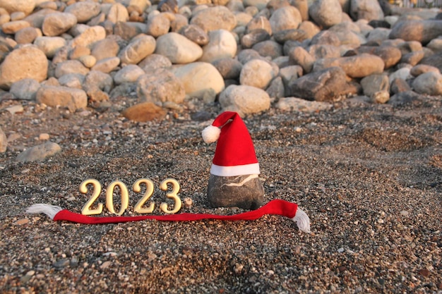 2023 números dorados y sombrero de santa en una piedra en la playa Concepto de año nuevo