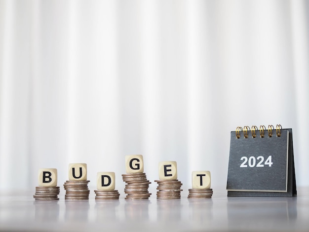 2024-Tischkalender und Holzblöcke mit dem Wort BUDGET auf einem Stapel Münzen Das Konzept der Budgetplanung und -zuweisung im Jahr 2024