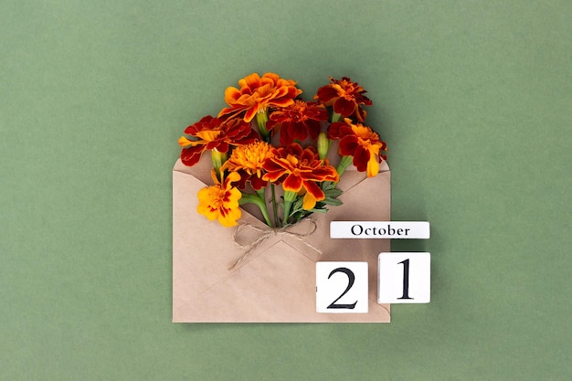 21. Oktober Blumenstrauß aus orangefarbener Blume in Bastelumschlag und Kalenderdatum auf grünem Hintergrund Minimales Konzept Hallo Herbst Vorlage für Ihre Design-Grußkarte