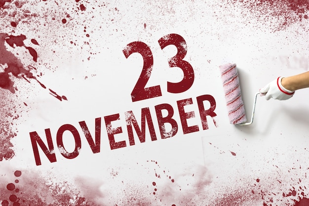 23.11. Tag 23 des Monats, Kalenderdatum. Die Hand hält eine Rolle mit roter Farbe und schreibt ein Kalenderdatum auf einen weißen Hintergrund. Herbstmonat, Tag des Jahreskonzepts.