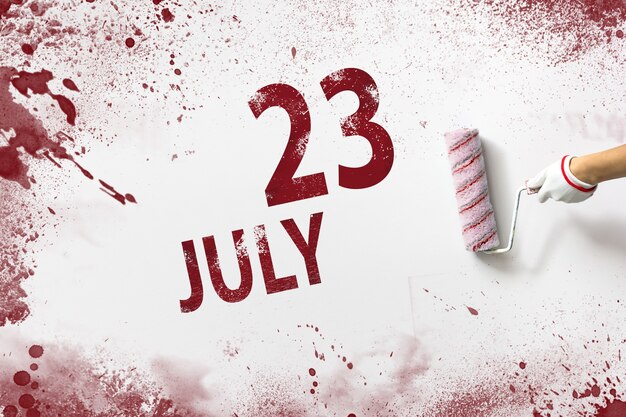 23. Juli. Tag 23 des Monats, Kalenderdatum. Die Hand hält eine Rolle mit roter Farbe und schreibt ein Kalenderdatum auf einen weißen Hintergrund. Sommermonat, Tag des Jahreskonzepts.