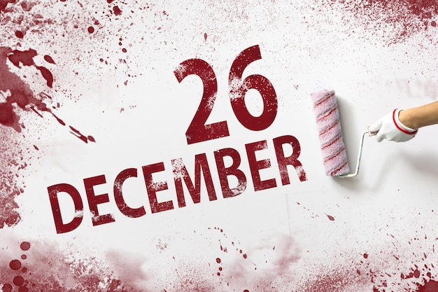 26 de diciembre. Día 26 del mes, fecha del calendario. La mano sostiene un rodillo con pintura roja y escribe una fecha del calendario sobre un fondo blanco. Mes de invierno, concepto de día del año.