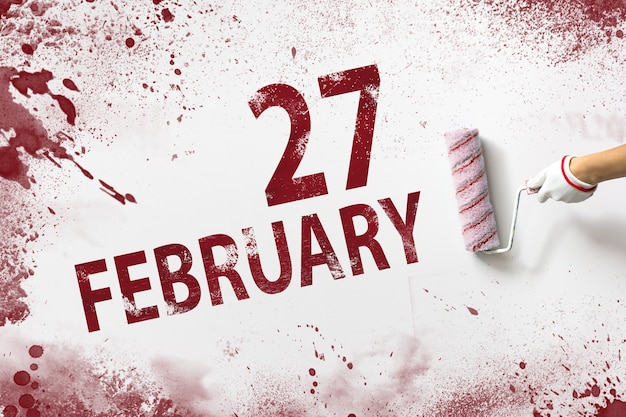 Foto 27. februar. tag 27 des monats, kalenderdatum. die hand hält eine rolle mit roter farbe und schreibt ein kalenderdatum auf einen weißen hintergrund. wintermonat, tag des jahreskonzepts.
