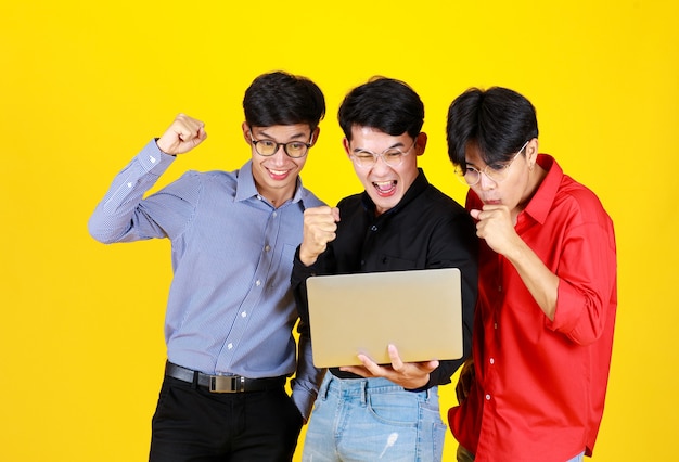 3 adultos asiáticos bonitos homens e 1 deles segurando laptop na mão. Todos eles usando óculos e levantando o punho parecem animados com a felicidade de sentir algo no laptop. No conceito de equipe com sucesso.