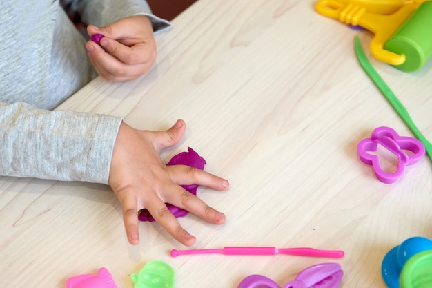 3 años niña artes creativas. Manos de niño jugando con plastilina de arcilla de colores. Autoaislamiento Covid-19, educación en línea, educación en el hogar. Niña pequeña estudiando en casa, aprendizaje en casa.