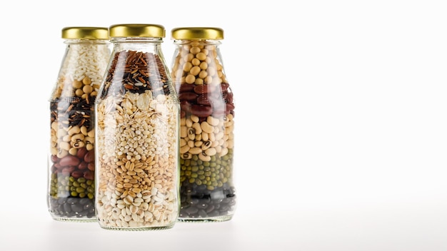 3 botellas de vidrio transparente contienen granos de cereales orgánicos limpios, semillas, cultivos secos, frijoles, arroz como ingredientes crudos y una receta de material de cocina vegana saludable y menú de bebidas de compuestos naturales mixtos