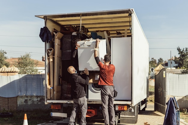 3 colegas de uma empresa de mudanças carregam uma máquina de lavar louça no caminhão