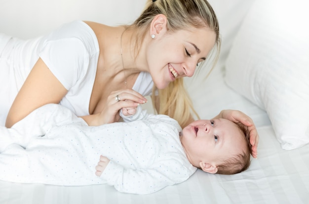 3 Monate altes Baby, das mit junger lächelnder Mutter auf dem Bett liegt