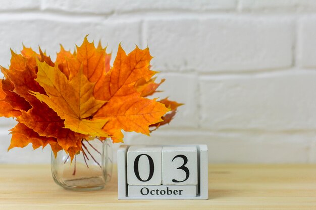 3 de octubre en el calendario y un ramo de hojas de otoño brillantes en la mesa. Uno de los días del mes de otoño. Calendario de octubre. El concepto del otoño dorado.