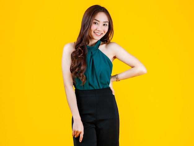 30 años linda y encantadora morena mujer asiática de pelo rizado posan para la cámara con un gesto alegre y positivo con fines publicitarios. Tomada con flash de estudio aislado sobre fondo amarillo.