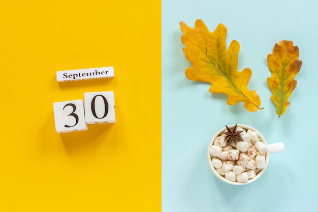 30 de setembro, xícara de chocolate com marshmallows e folhas de outono amarelas sobre fundo azul amarelo.