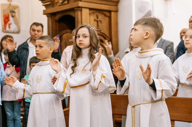 300523 Vinnitsa Ukraine Porträts von Kindern, die ihre erste Kommunion in einer katholischen Kirche erhalten, der Priester segnet sie