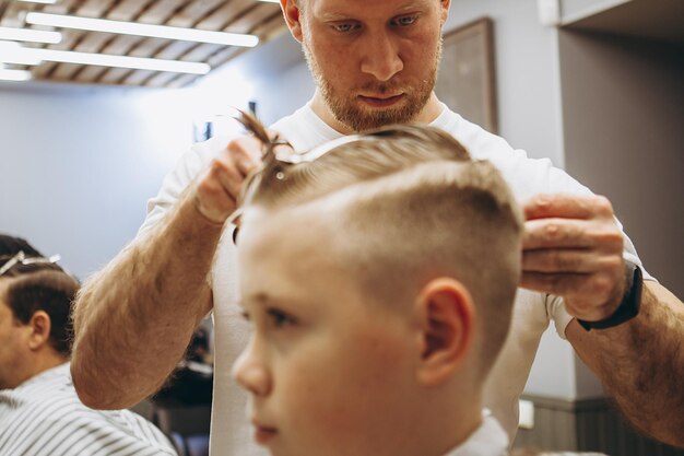 30112019 Vinnitsa Ukraine süßer Vorschuljunge bekommt einen Haarschnitt Kinderfriseur mit Schere und Kamm schneidet kleinen Jungen im Friseursalon mit Loft-Interieur