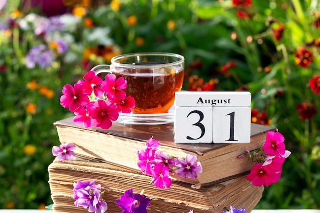 31 de agosto Xícara de chá e data de calendário na pilha de livros contra fundo floral brilhante dia ensolarado de verão