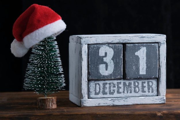 Foto 31 de diciembre en el calendario de madera de pie junto al árbol de navidad decorado con sombrero de santa claus