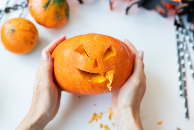 31. Oktober. Halloween-Feiertag. Das Mädchen hält das geschnitzte Gesicht eines Kürbisses in den Händen. Sicht von oben.