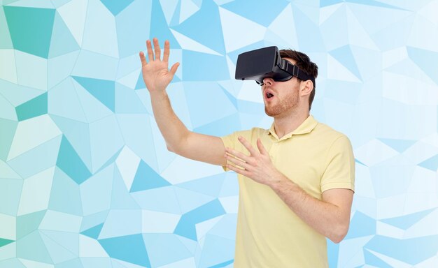3D-Technologie, Virtual Reality, Entertainment und People-Konzept - überraschter junger Mann mit Virtual-Reality-Headset oder 3D-Brille, der ein Spiel über Low-Poly-Hintergrund spielt
