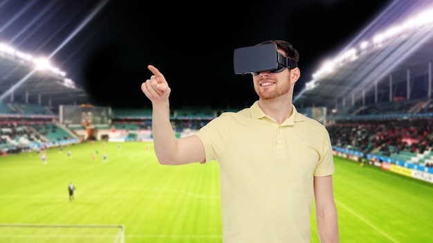 3D-Technologie, Virtual Reality, Sport, Unterhaltung und People-Konzept - glücklicher junger Mann mit Virtual-Reality-Headset oder 3D-Brille, der ein Spiel über dem Fußballplatz im Stadionhintergrund spielt