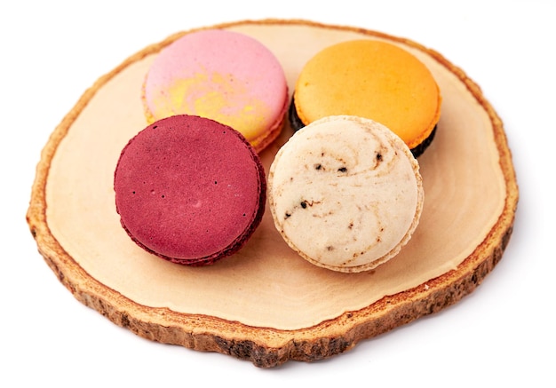 4 bunte Macarons in Rosa, Rot, Orange und Cremebraun auf einem Holzteller isoliert auf weißem Hintergrund