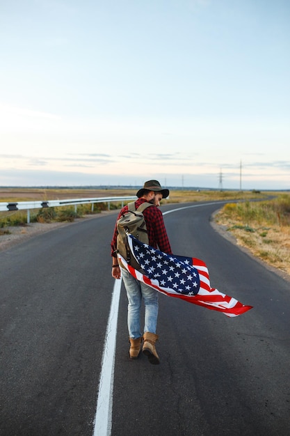 4 de Julho Bandeira Americana Viajante com a bandeira da América O homem com um chapéu uma camisa de mochila