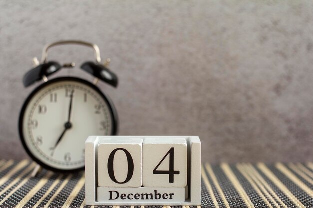 4. Dezember auf einem Holzkalender neben einem Wecker auf einem dunklen Tisch Ein Tag im WinterPlatz für Text