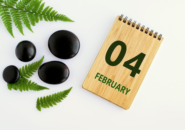 4. Februar 04. Tag des Monats Kalenderdatum Notizblock schwarze Steine grüne Blätter Wintermonat das Konzept des Tages des Jahres