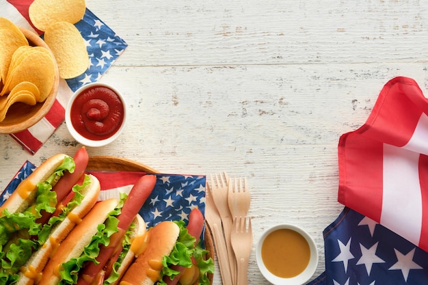4. Juli, amerikanischer Unabhängigkeitstag, traditionelles Picknick-Essen, Hot Dog mit Kartoffelchips und Cocktail, amerikanische Flaggen und Symbole der USA, patriotischer Picknick-Feiertag auf weißem Holzhintergrund, Draufsicht