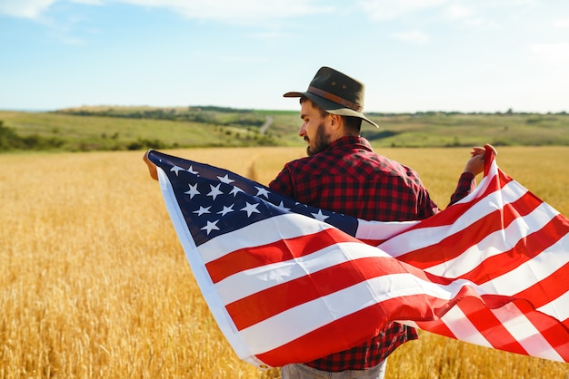 Foto 4. juli. vierter juli. amerikaner mit der nationalflagge. amerikanische flagge. tag der unabhängigkeit. patriotischer urlaub. der mann trägt einen hut, einen rucksack, ein hemd und jeans.