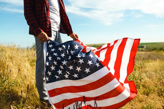 4. Juli. Vierter Juli. Amerikaner mit der Nationalflagge. Amerikanische Flagge. Tag der Unabhängigkeit. Patriotischer Urlaub. Der Mann trägt einen Hut, einen Rucksack, ein Hemd und Jeans.