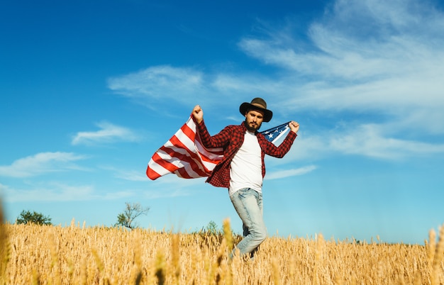 4 de julio. Cuatro de Julio. Americano con la bandera nacional. Bandera estadounidense. Día de la Independencia. Fiesta patriótica. El hombre lleva un sombrero, una mochila, una camisa y jeans.