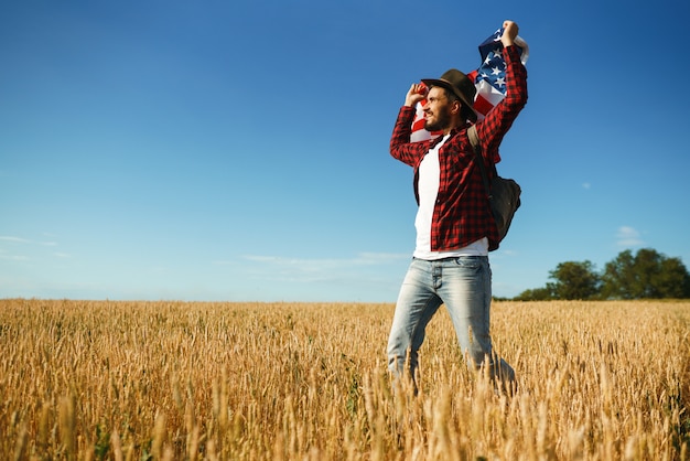 4 de julio. Cuatro de Julio. Americano con la bandera nacional. Bandera estadounidense. Día de la Independencia. Fiesta patriótica. El hombre lleva un sombrero, una mochila, una camisa y jeans.