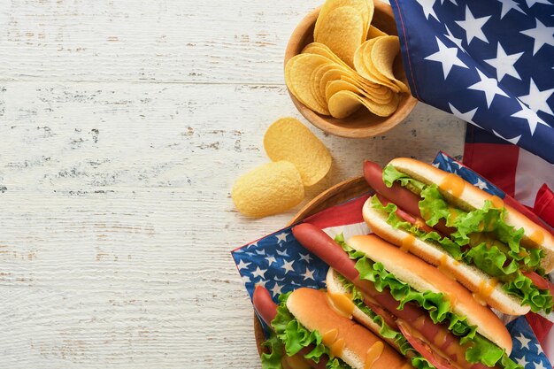 4 de julio Día de la Independencia de Estados Unidos comida de picnic tradicional Perro caliente con papas fritas y cóctel Banderas y símbolos estadounidenses de vacaciones de picnic patriótico de EE. UU. Sobre fondo de madera blanca Vista superior